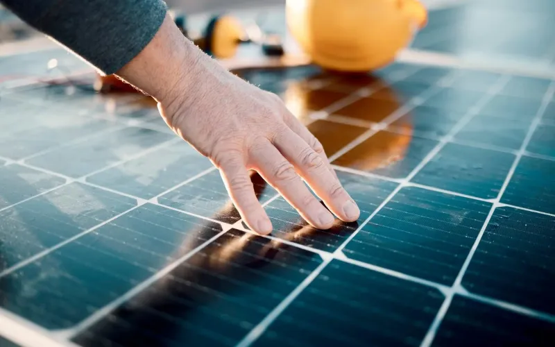 Primo piano della mano di un installatore che controlla un pannello fotovoltaico sul tetto.